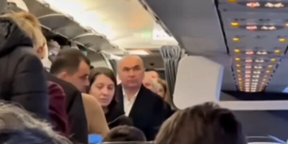 Summitul de la Londra. Ilie Bolojan, filmat într-un avion de linie, la clasa economic – preşedintele interimar a ajutat un alt pasager să-şi aşeze valiza